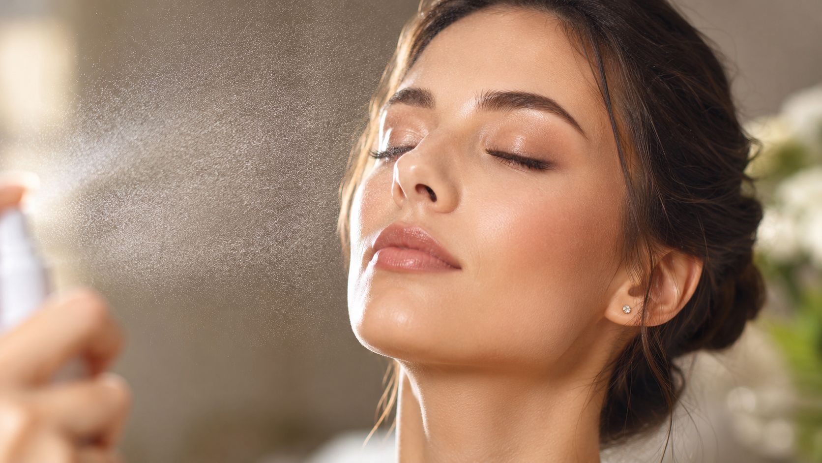 A young woman with her eyes closed, refreshing her skin with a light facial setting spray mist.