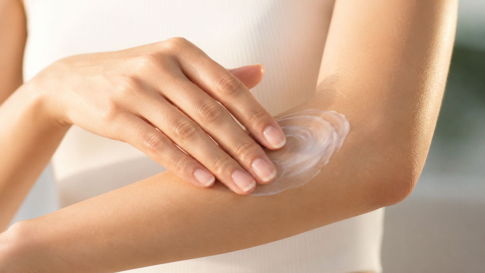 A close-up view of a person applying white moisturizing cream to their arm in a circular motion.
