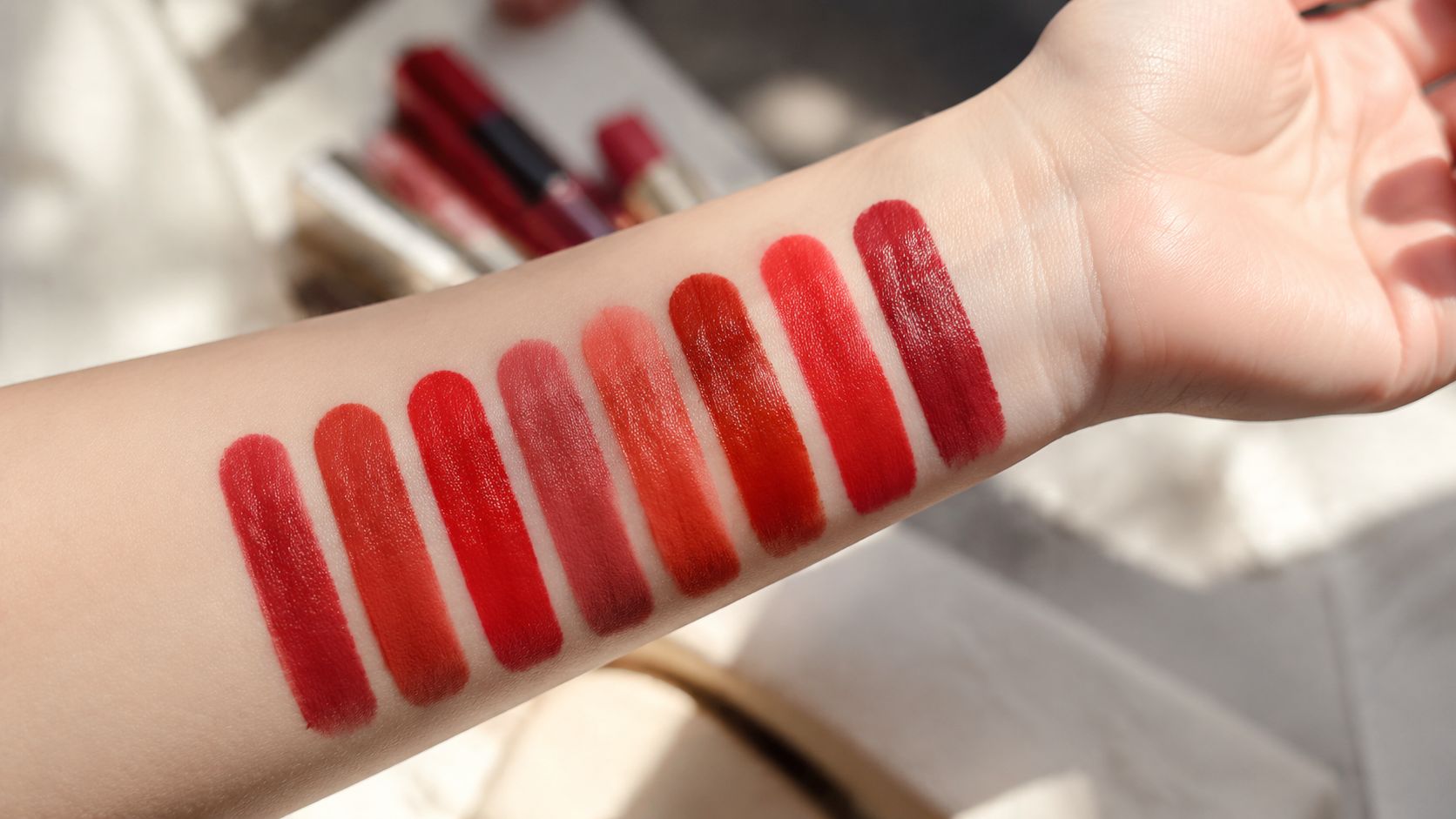 A forearm displaying eight vibrant shades of red lipstick swatches in a row under bright lighting.