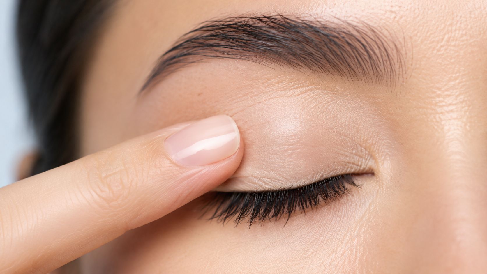 A close-up view of a person applying primer to their eyelid with a finger before makeup.