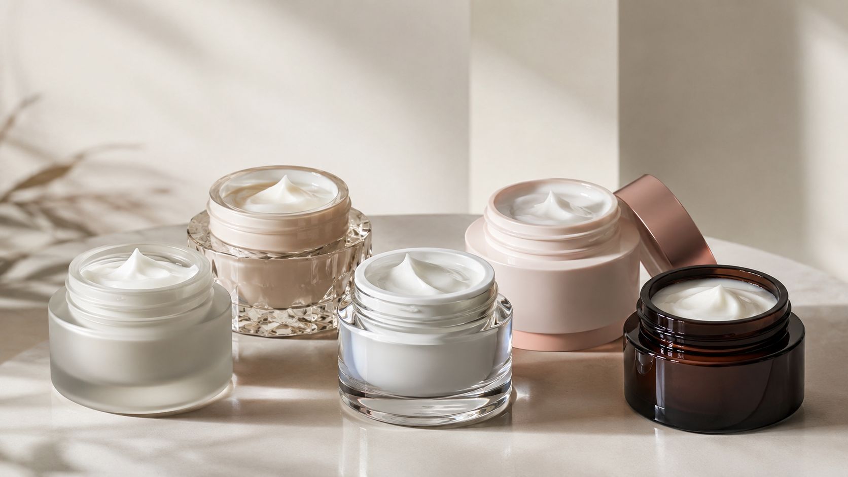 An arrangement of luxury glass cosmetic jars containing moisturizing face cream on a neutral stone surface.