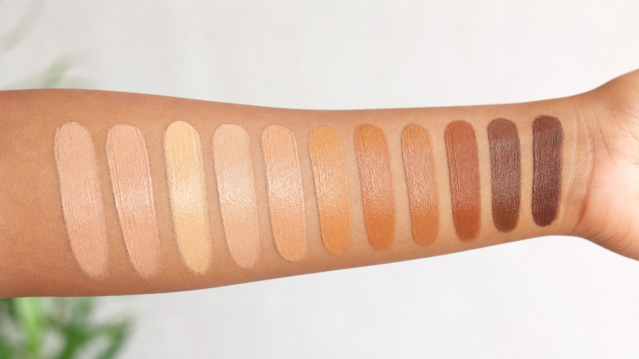A close-up shot of eleven different skin-toned foundation swatches painted on a person's inner forearm.