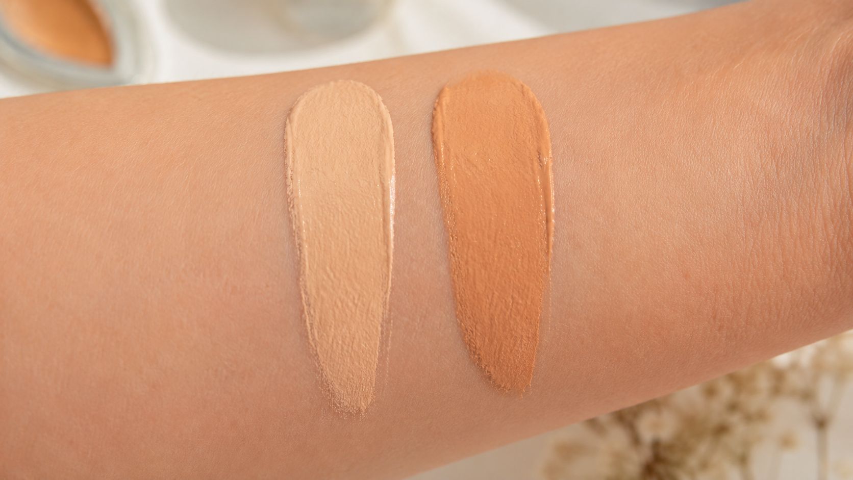 Two distinct makeup foundation shades swatched side-by-side on a person's inner arm for color comparison.