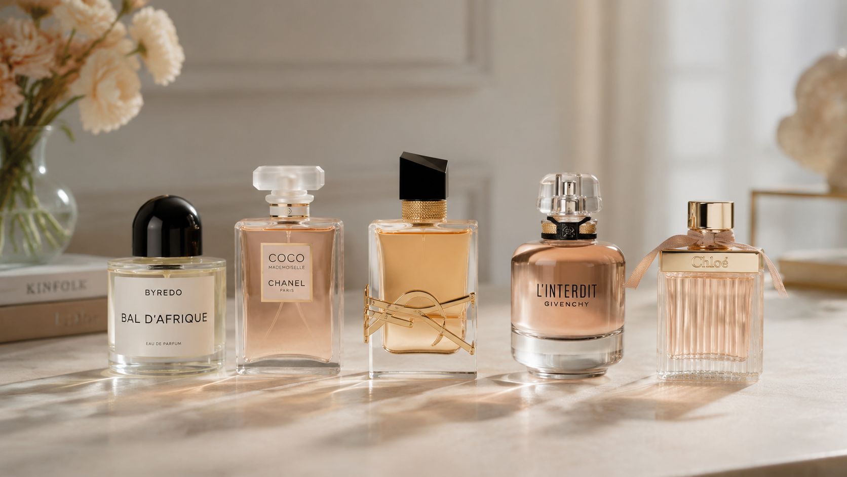 A collection of five luxury designer perfume bottles arranged on a marble surface near a floral vase.