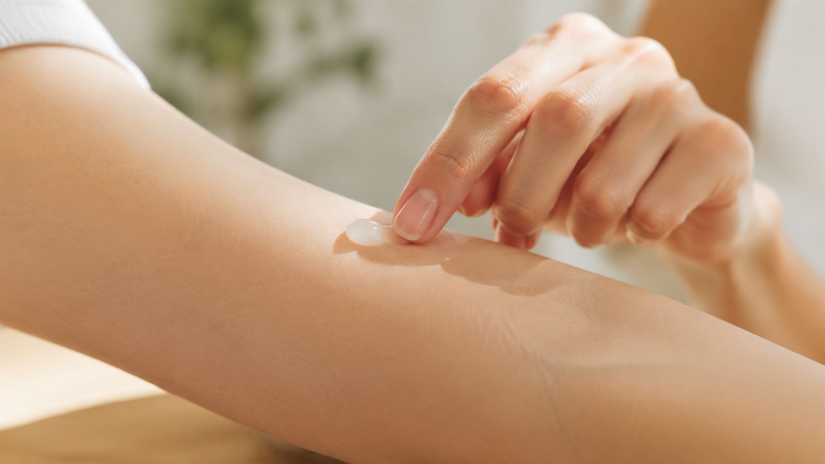 A close-up view of a person applying a small amount of cream onto their forearm with a finger.