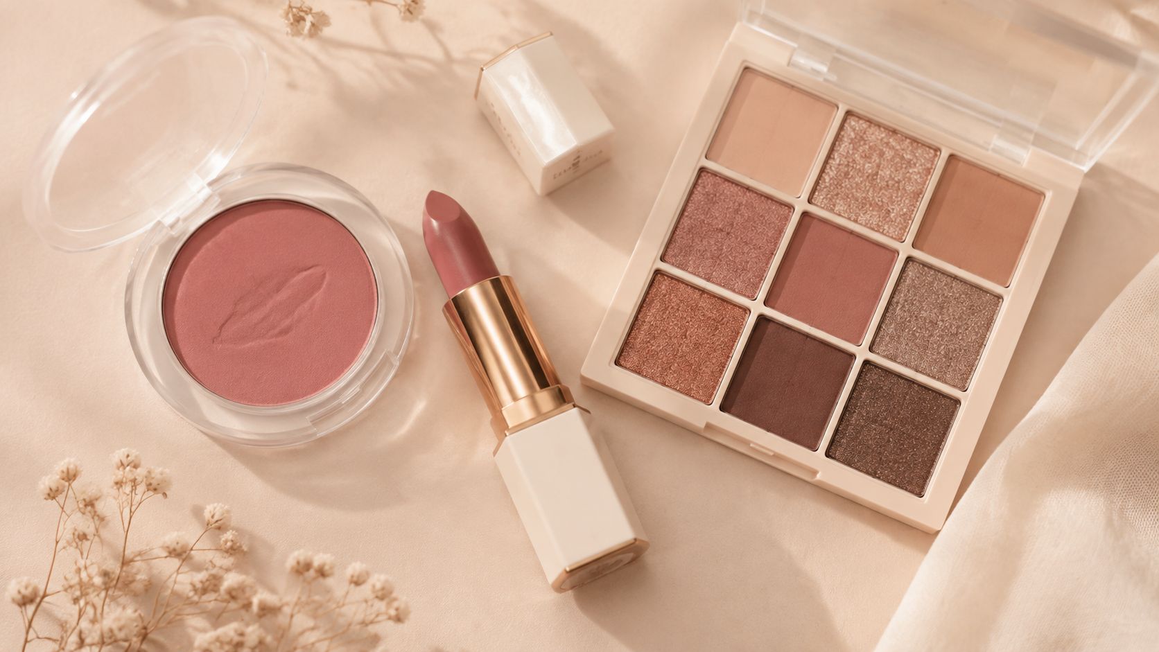 A beautiful collection of rosy mauve lipstick, eyeshadow palette, and blush on a light beige background.