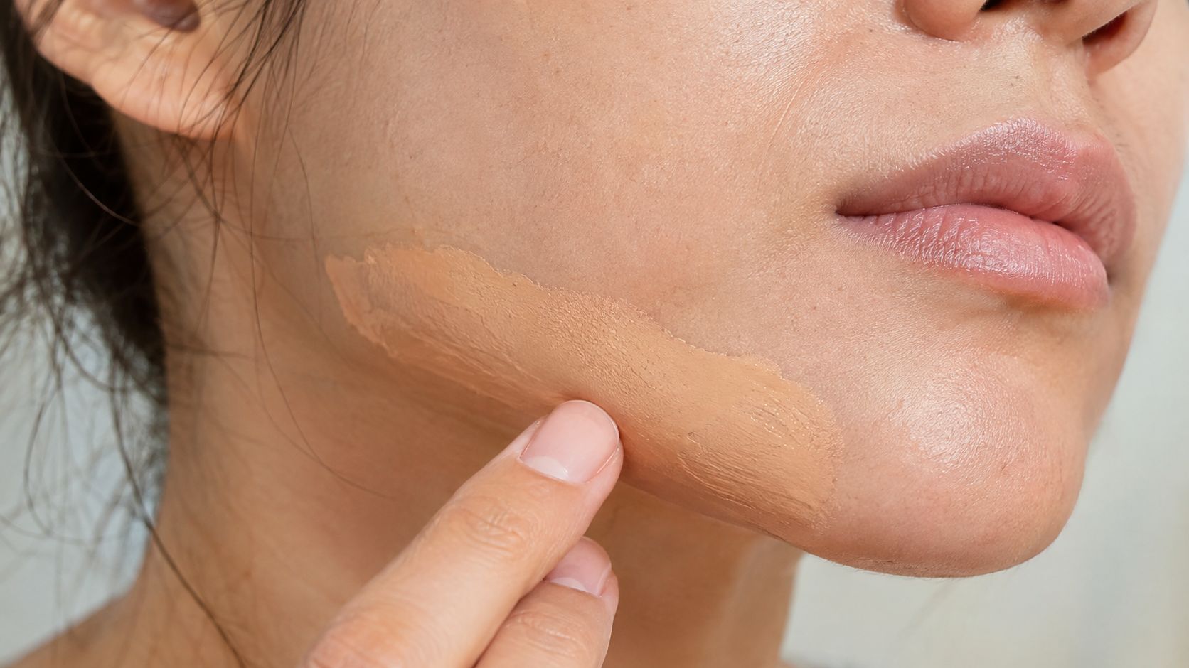 A close-up view of a person applying foundation to their cheek for an undertone color match test.