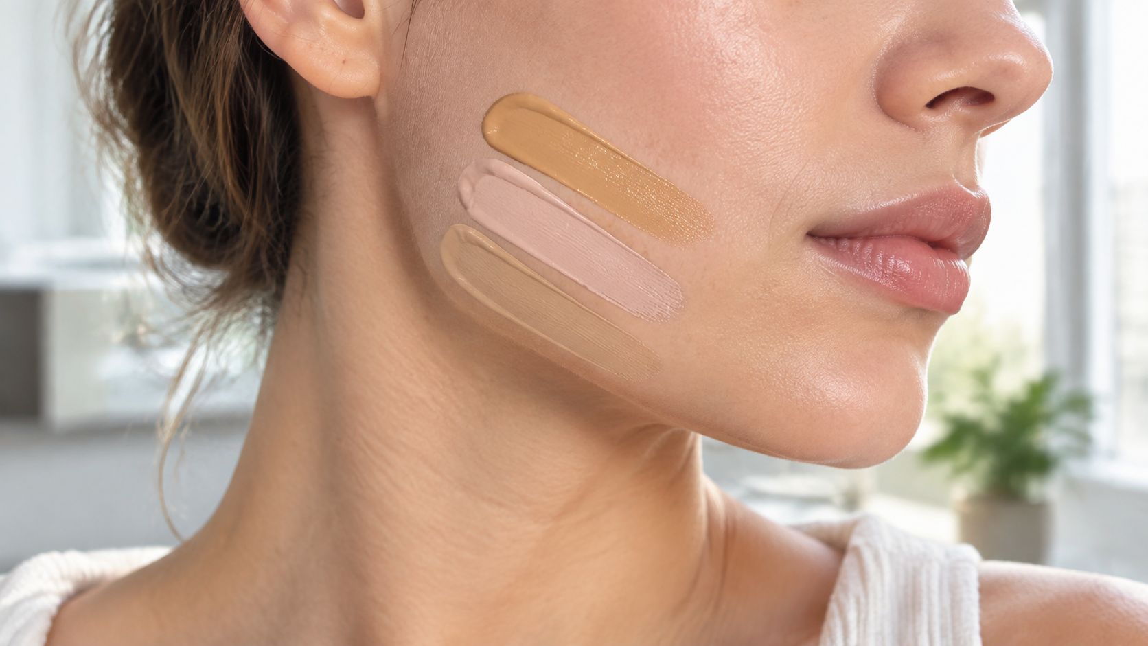 A close-up view of a woman testing three different shades of foundation on her cheek area.
