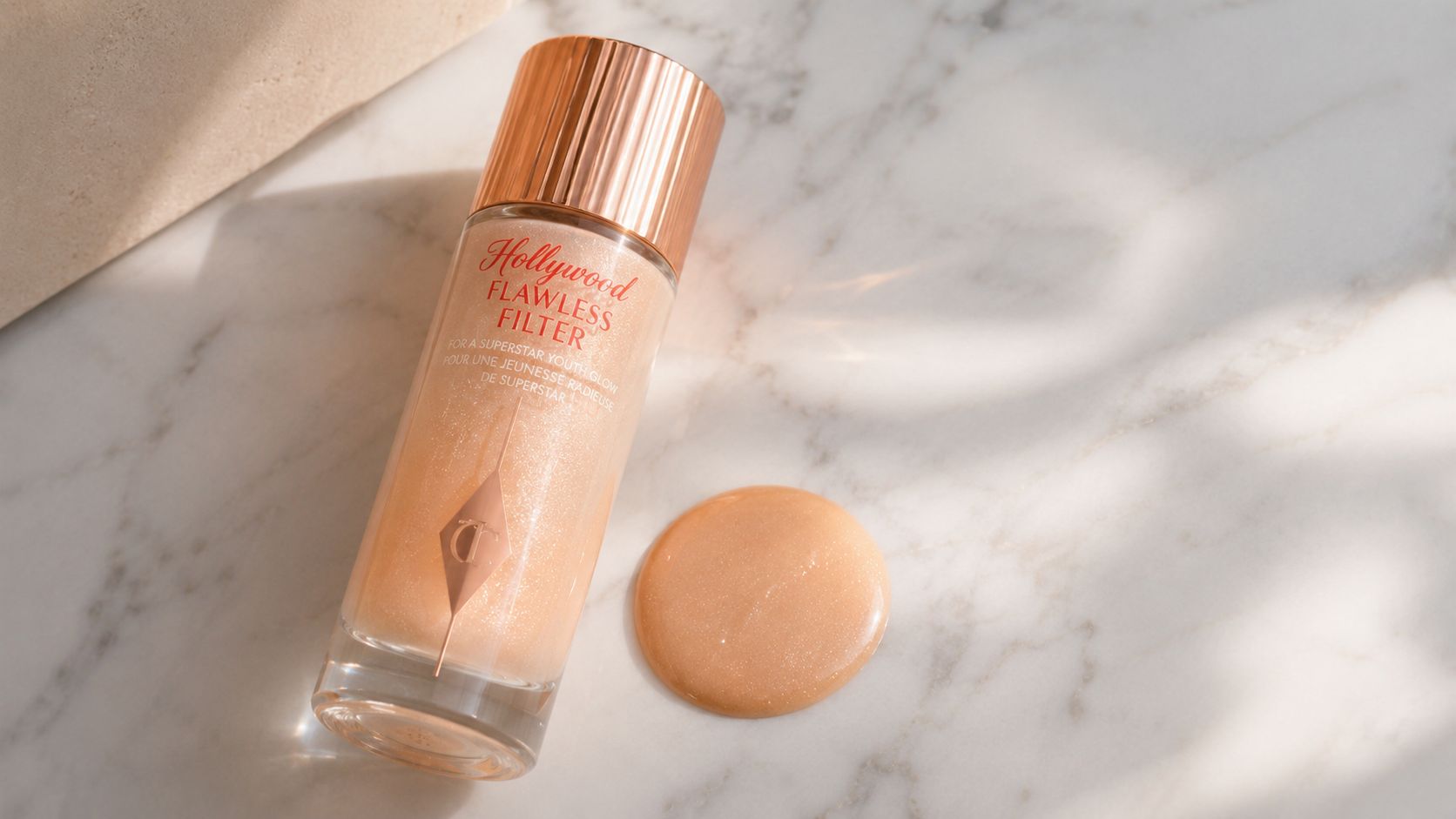 A glass bottle of Charlotte Tilbury Hollywood Flawless Filter foundation next to a smear of product.