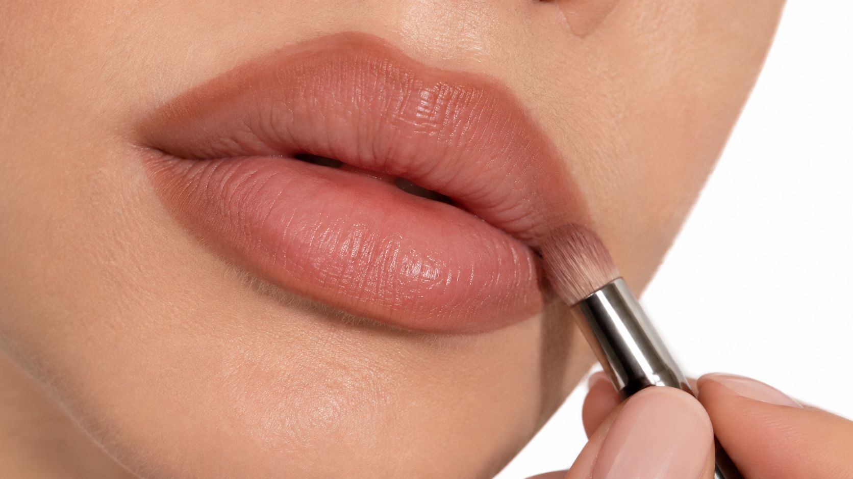 A close-up shot of a makeup brush applying subtle nude lip liner to perfectly defined lips.