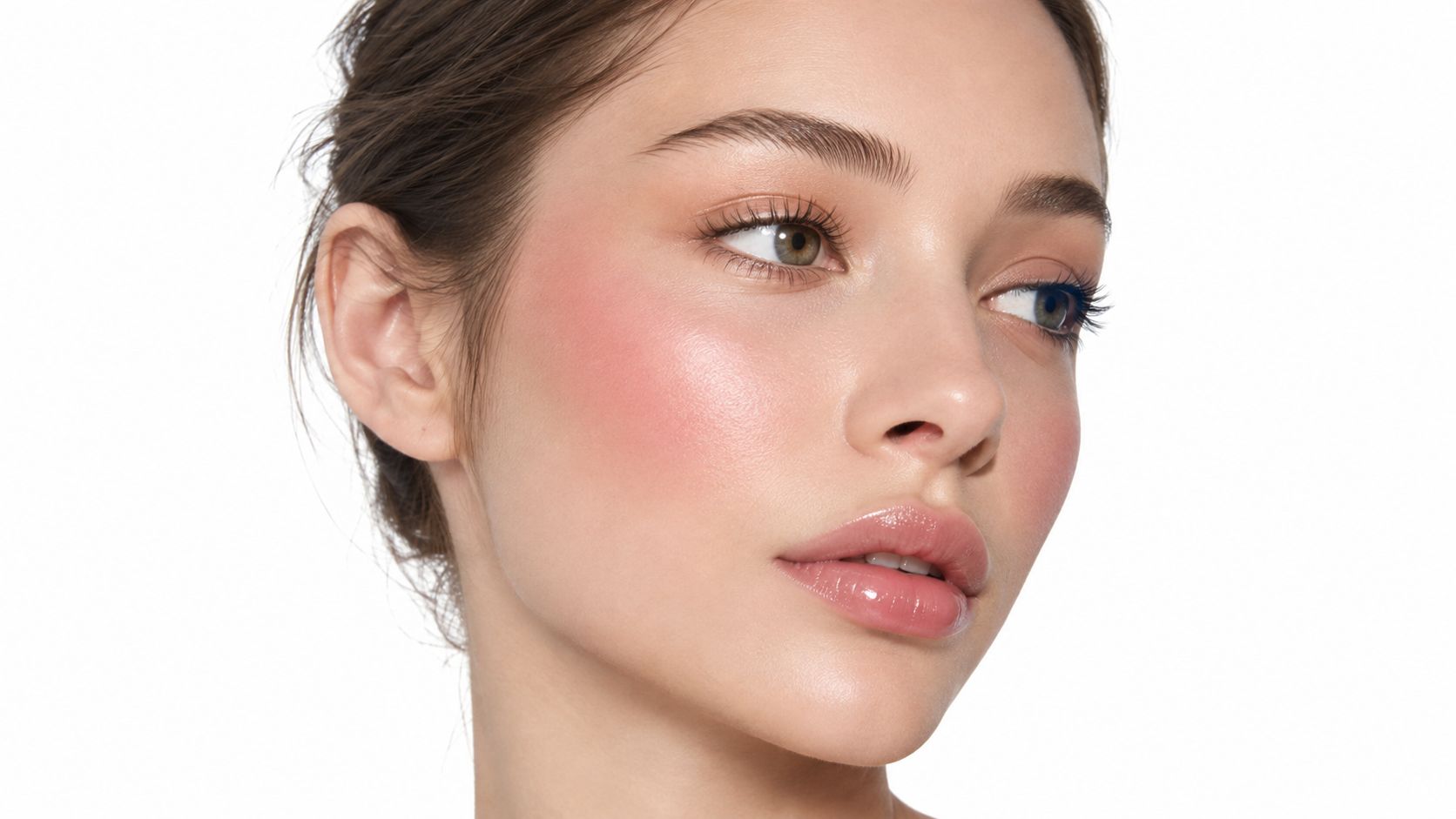 A close up portrait of a young woman with glowing skin wearing soft pink blush