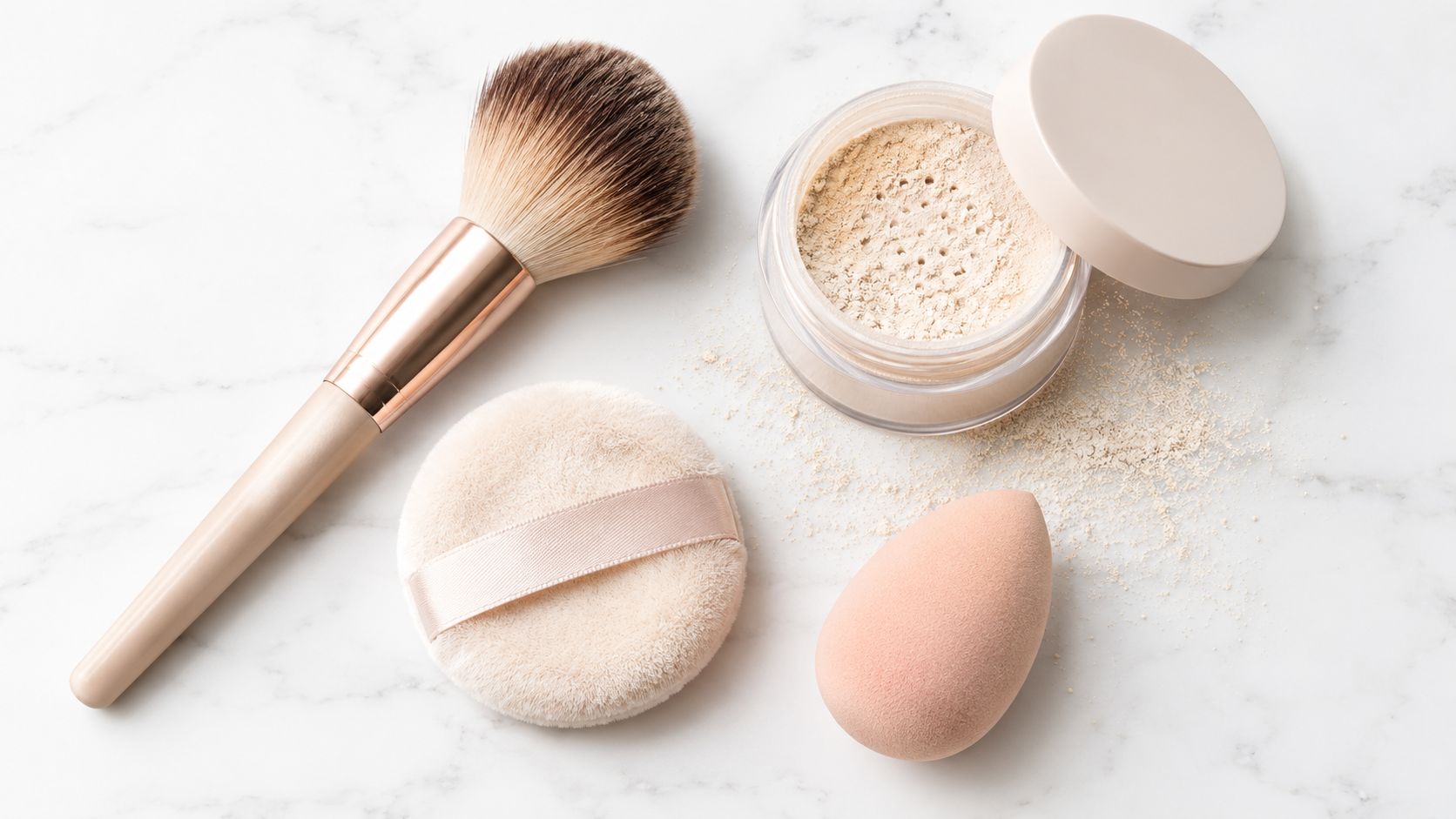 A professional makeup brush, a soft powder puff, and a makeup sponge next to loose face powder.