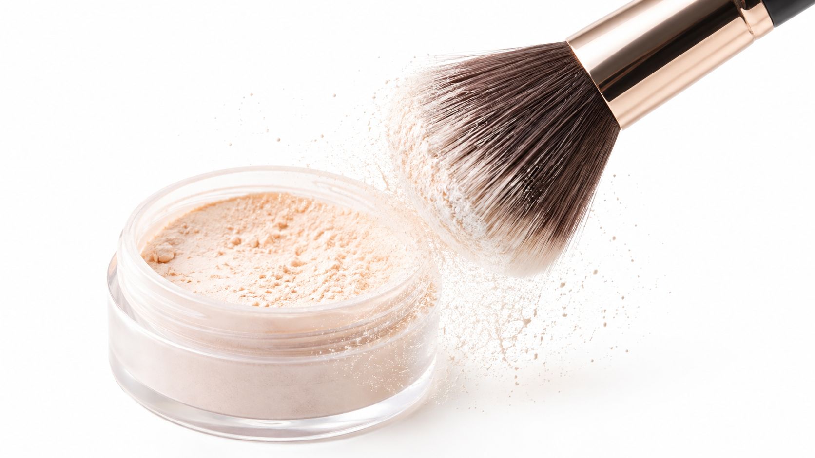 A soft makeup brush applying loose translucent powder from a clear cosmetic jar onto a white surface.