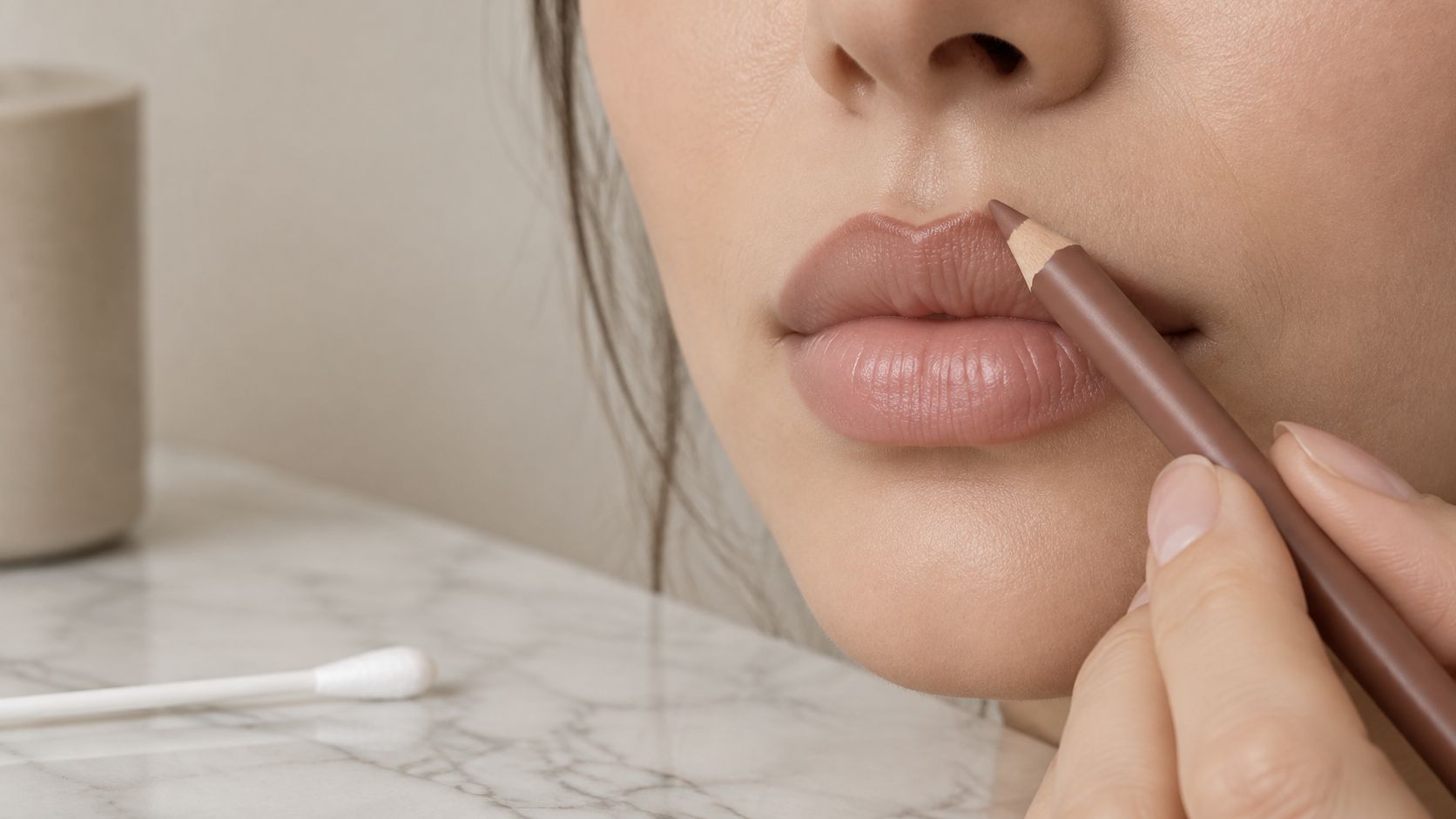 A close-up view of a person applying brown lip liner to outline their lips for makeup.